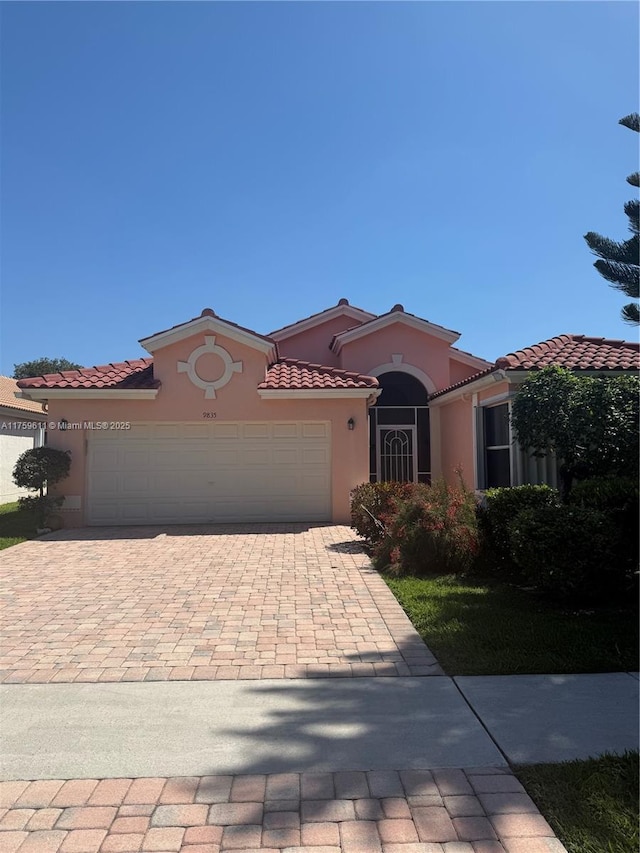 mediterranean / spanish house with a tile roof, decorative driveway, a garage, and stucco siding