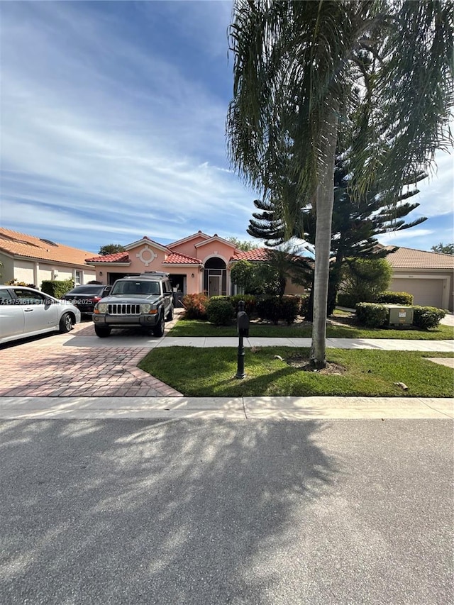 view of front facade with an attached garage, a tiled roof, decorative driveway, stucco siding, and a front yard