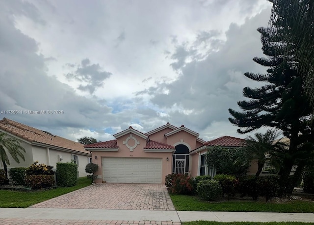 mediterranean / spanish house with stucco siding, a tiled roof, decorative driveway, and a garage