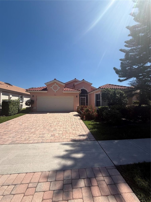 view of front of home with a tile roof, decorative driveway, an attached garage, and stucco siding