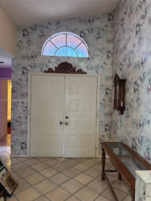 entrance foyer featuring a textured ceiling, light tile patterned floors, and wallpapered walls