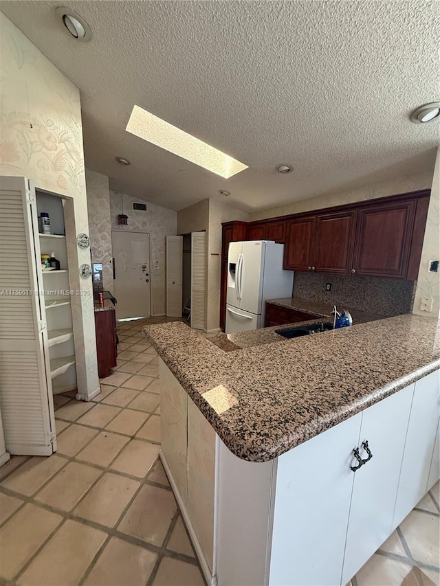 kitchen featuring a textured ceiling, a peninsula, white refrigerator with ice dispenser, a sink, and lofted ceiling with skylight