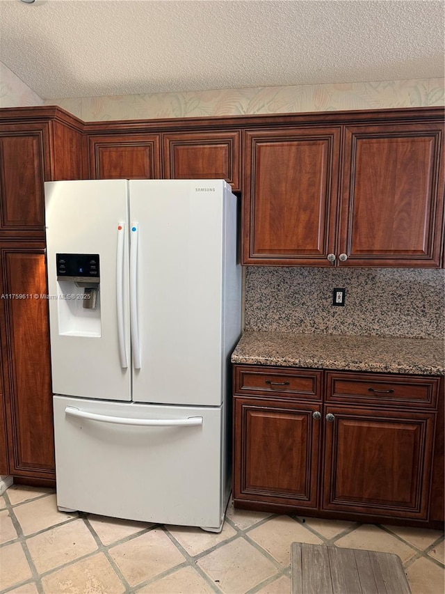 kitchen with a textured ceiling, white refrigerator with ice dispenser, decorative backsplash, dark stone counters, and light floors