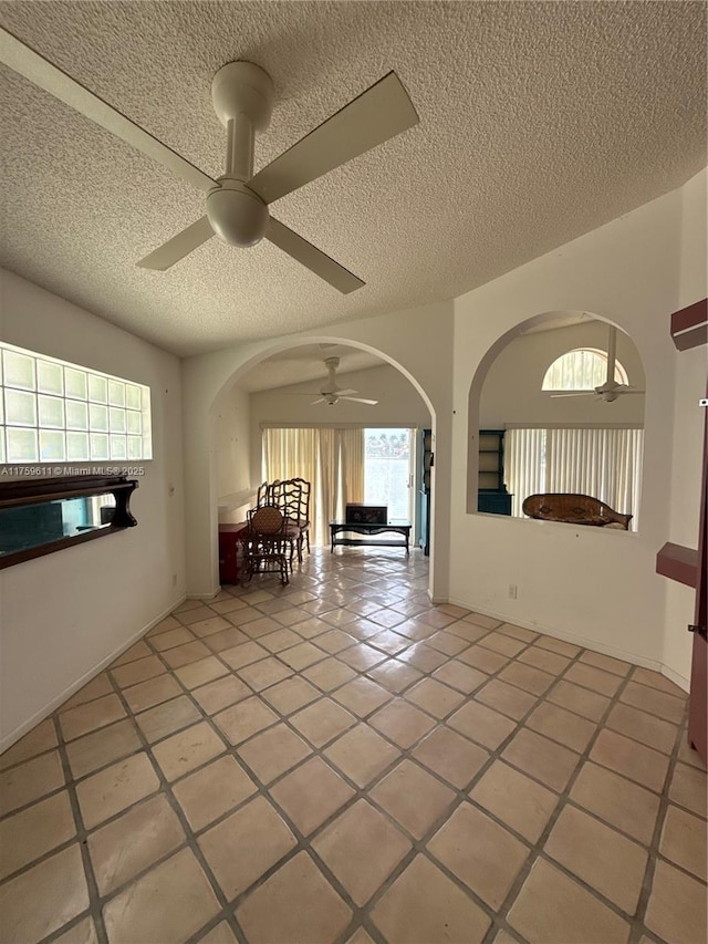 interior space with a ceiling fan, arched walkways, a textured ceiling, and light tile patterned floors