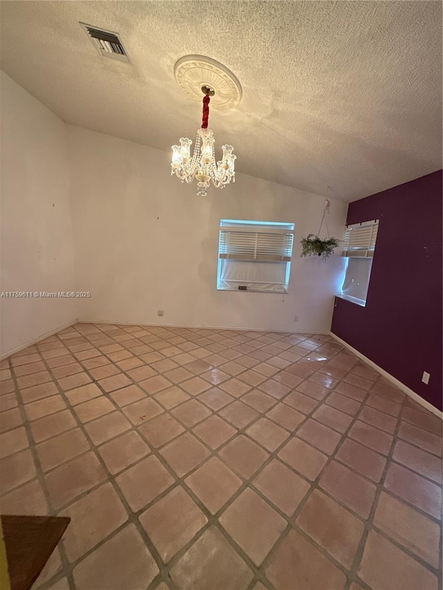 spare room featuring lofted ceiling, a textured ceiling, visible vents, and a notable chandelier