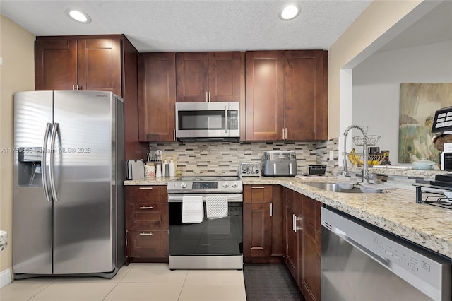 kitchen featuring light tile patterned floors, light stone counters, a sink, appliances with stainless steel finishes, and backsplash