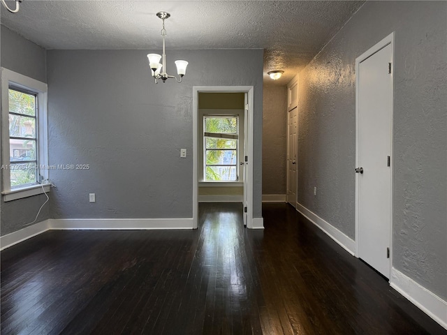 empty room featuring wood-type flooring, baseboards, a textured ceiling, and a textured wall