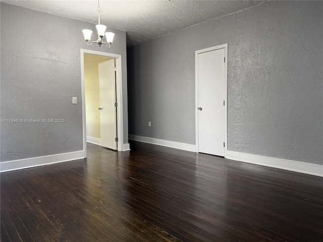 spare room with an inviting chandelier, baseboards, wood finished floors, and a textured wall