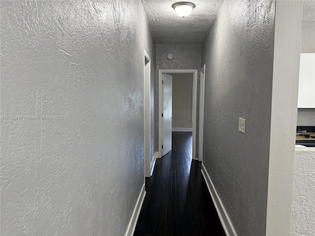 corridor featuring a textured wall, a textured ceiling, baseboards, and wood finished floors