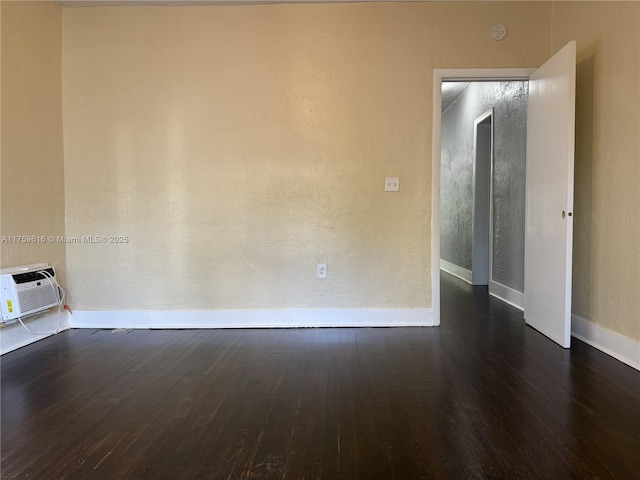 empty room with a wall unit AC, wood finished floors, and baseboards