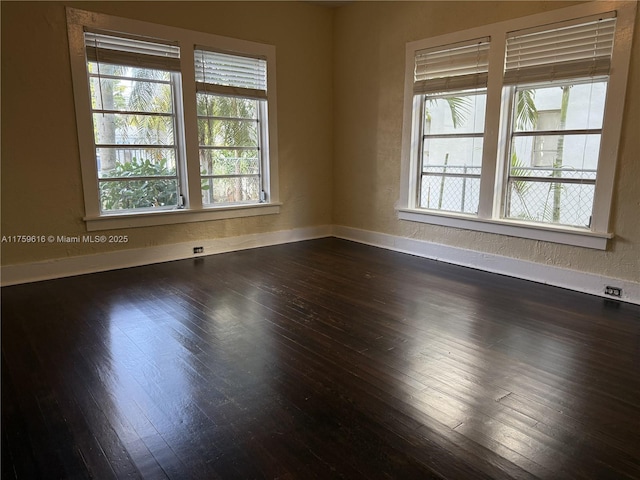 empty room featuring dark wood-style floors, a textured wall, and baseboards