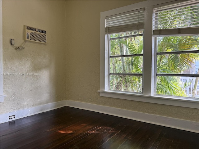 unfurnished room featuring dark wood finished floors, a wall unit AC, a textured wall, and baseboards