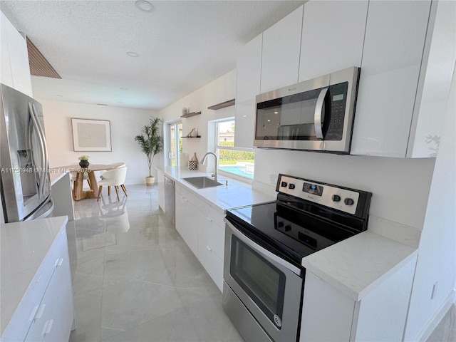 kitchen featuring marble finish floor, modern cabinets, a sink, white cabinetry, and stainless steel appliances