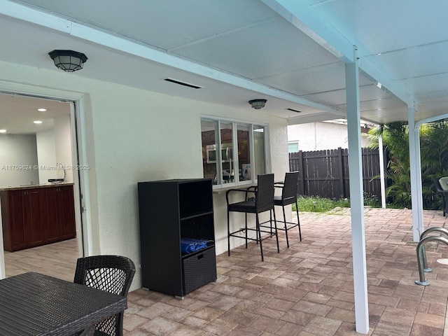 view of patio with outdoor dry bar and fence