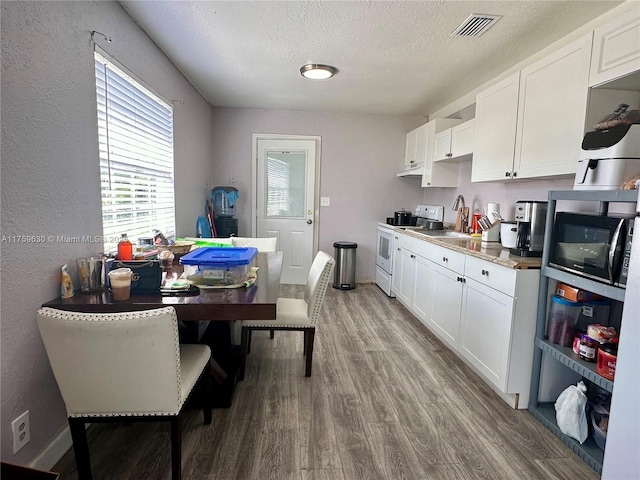 kitchen with electric range, visible vents, wood finished floors, white cabinets, and black microwave