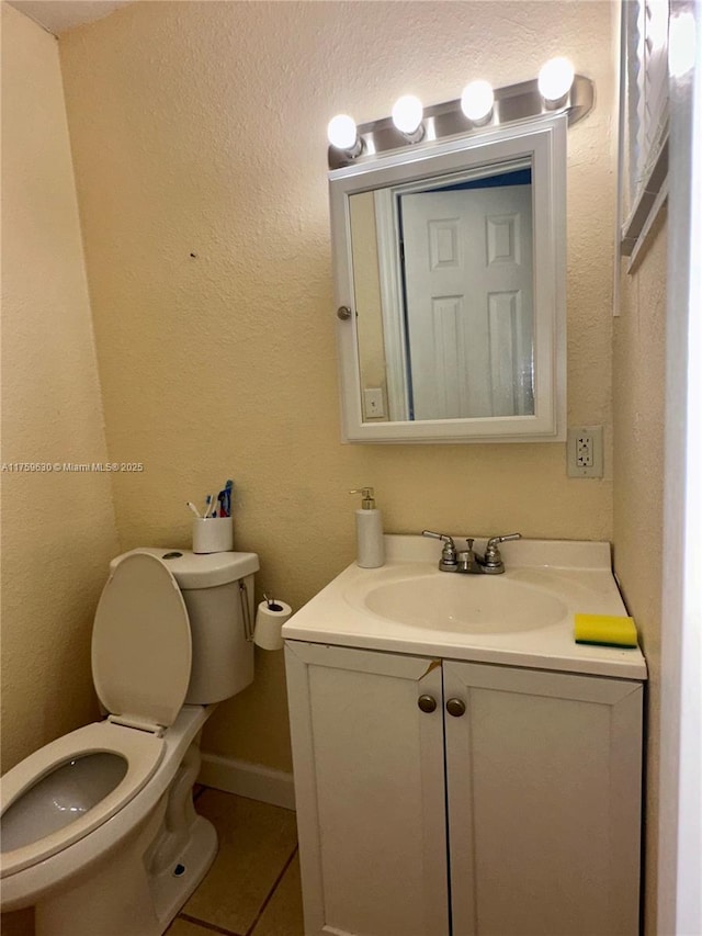 half bath featuring tile patterned flooring, toilet, vanity, and a textured wall