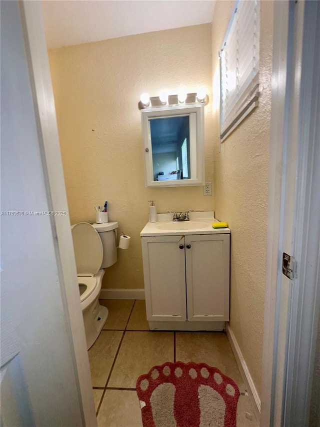 half bath featuring tile patterned floors, toilet, vanity, and baseboards