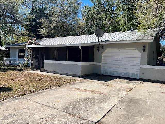 single story home featuring metal roof, an attached garage, a sunroom, concrete driveway, and a standing seam roof