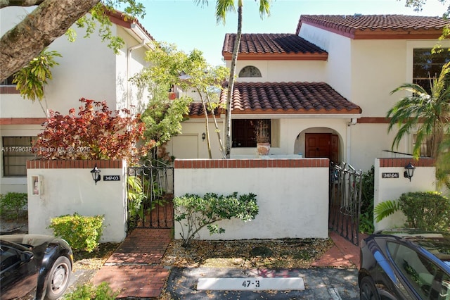 mediterranean / spanish home with a fenced front yard, stucco siding, a tiled roof, and a gate