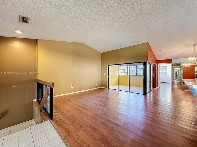 unfurnished living room with visible vents, a chandelier, vaulted ceiling, wood finished floors, and a textured ceiling