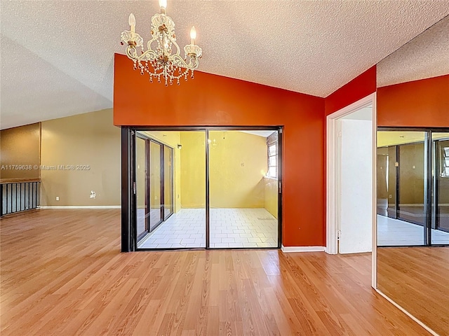 interior space featuring an inviting chandelier, vaulted ceiling, wood finished floors, and a textured ceiling