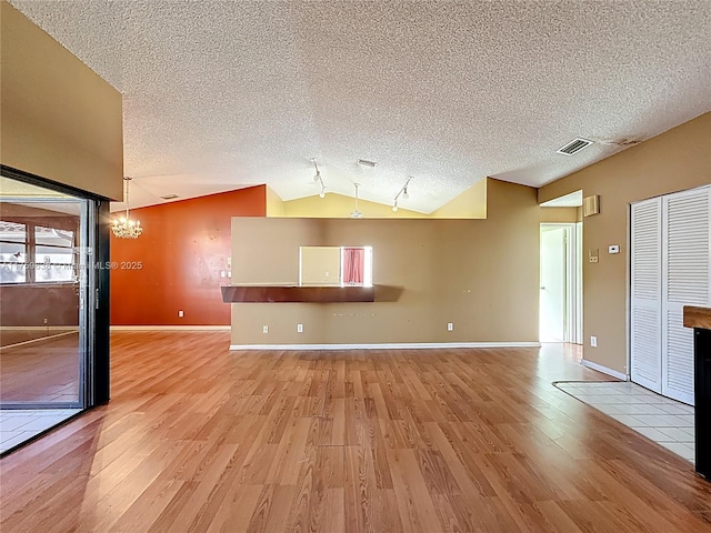 unfurnished living room featuring baseboards, visible vents, light wood-style flooring, vaulted ceiling, and a textured ceiling