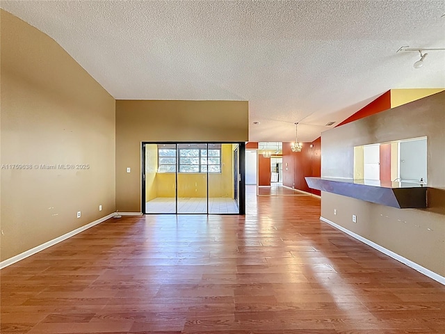 empty room featuring lofted ceiling, a notable chandelier, wood finished floors, and a textured ceiling