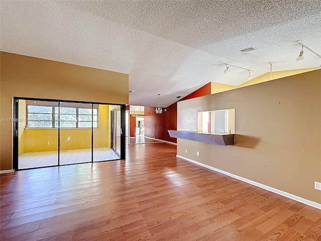 spare room featuring lofted ceiling, a textured ceiling, wood finished floors, and track lighting