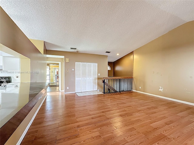 spare room featuring light wood-type flooring, baseboards, a textured ceiling, and visible vents