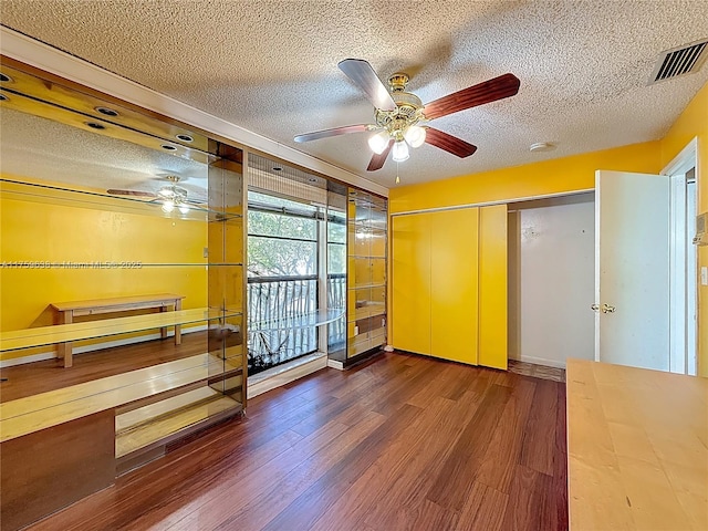 empty room with visible vents, a textured ceiling, wood finished floors, and a ceiling fan