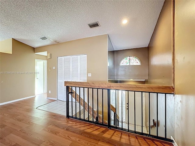 corridor featuring visible vents, an upstairs landing, a textured ceiling, and wood finished floors