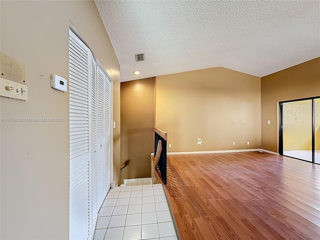 empty room featuring visible vents, a textured ceiling, wood finished floors, baseboards, and vaulted ceiling