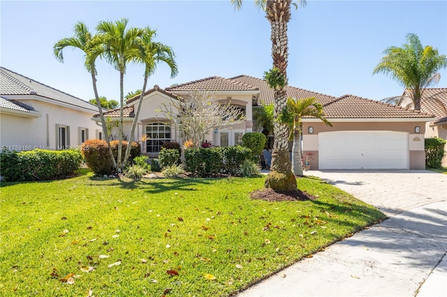 mediterranean / spanish-style home with an attached garage, a tiled roof, decorative driveway, stucco siding, and a front lawn