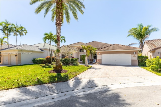 mediterranean / spanish home featuring driveway, a garage, a tile roof, a front yard, and stucco siding