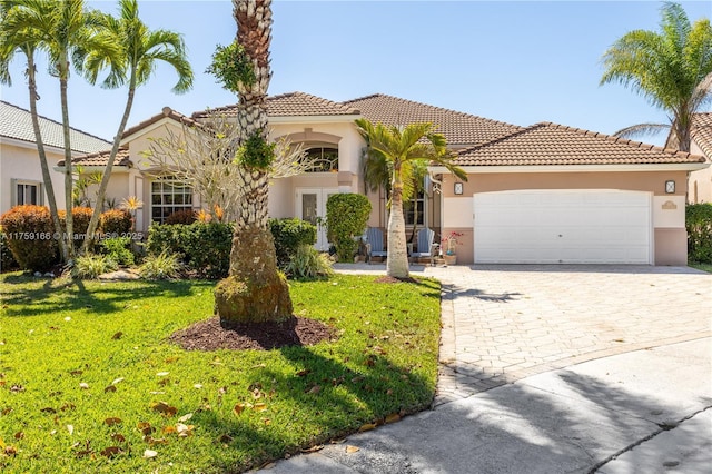 mediterranean / spanish-style home featuring stucco siding, an attached garage, decorative driveway, french doors, and a front yard