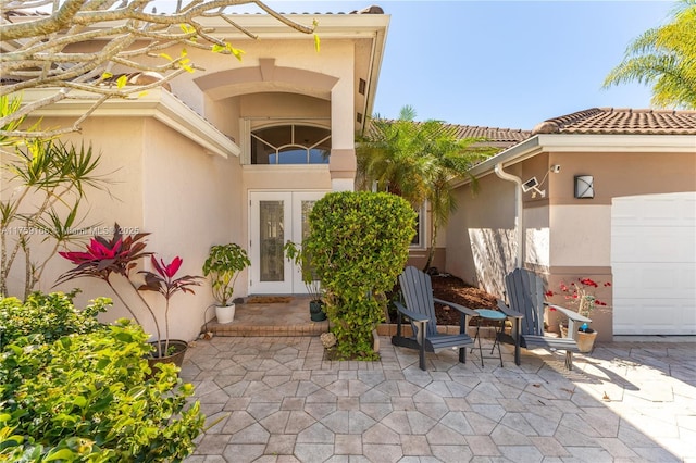 entrance to property featuring french doors, a tile roof, stucco siding, a patio area, and a garage