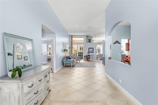 corridor with arched walkways, light tile patterned flooring, and baseboards