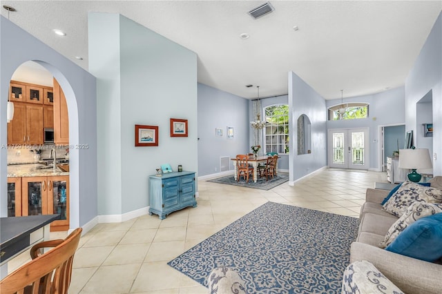 living room with arched walkways, french doors, light tile patterned floors, visible vents, and baseboards