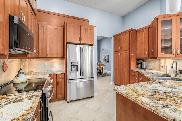 kitchen featuring light stone counters, arched walkways, light tile patterned floors, appliances with stainless steel finishes, and a sink