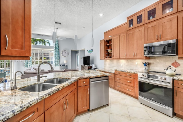 kitchen with brown cabinetry, decorative backsplash, light stone counters, appliances with stainless steel finishes, and a sink