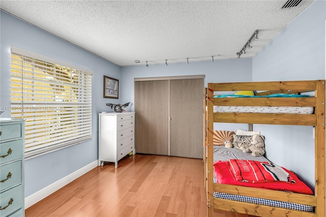 bedroom with a textured ceiling, visible vents, baseboards, light wood-style floors, and rail lighting