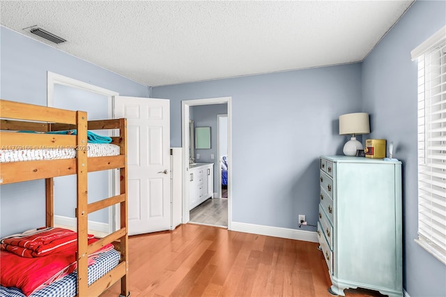 bedroom featuring baseboards, visible vents, connected bathroom, a textured ceiling, and light wood-type flooring