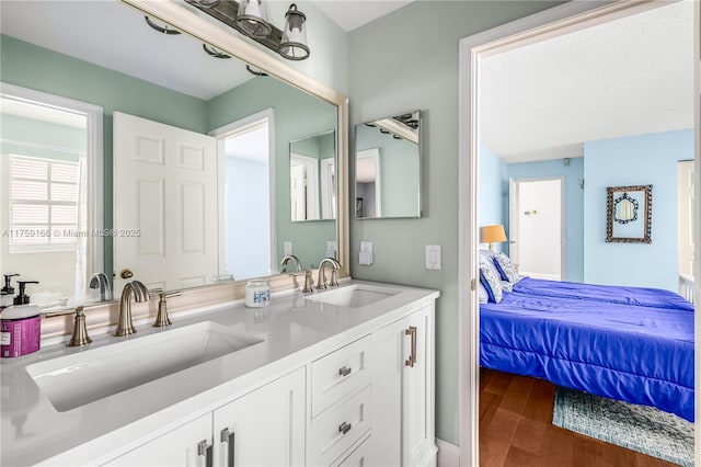 ensuite bathroom with double vanity, wood finished floors, a sink, and connected bathroom