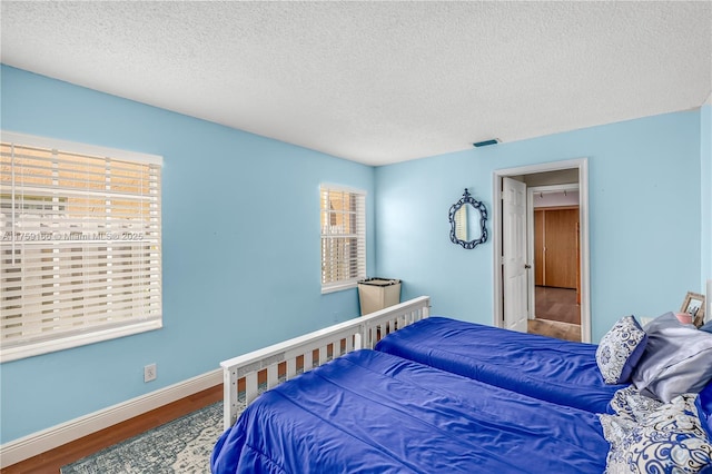 bedroom with visible vents, a textured ceiling, baseboards, and wood finished floors