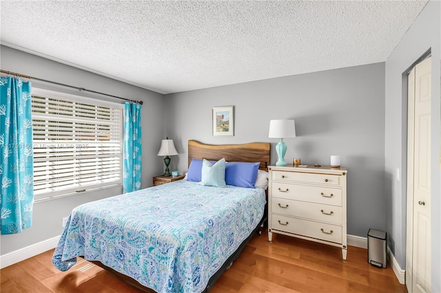 bedroom featuring a textured ceiling, baseboards, and wood finished floors