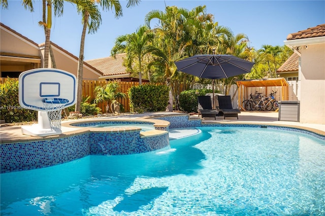 view of pool featuring a water slide, fence, and a pool with connected hot tub