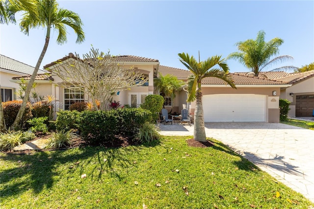 view of front of home with driveway, a garage, a tiled roof, a front lawn, and stucco siding