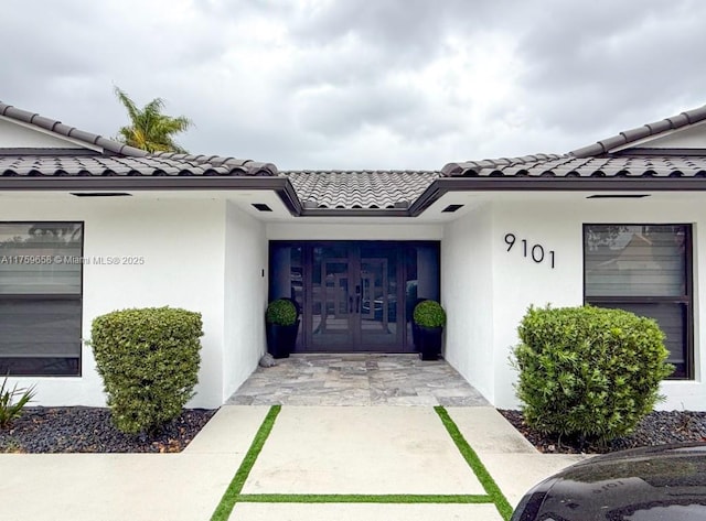 view of exterior entry with stucco siding and a tiled roof