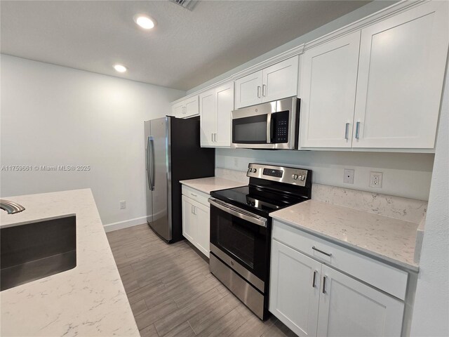 6001 Woods Edge Cir, Riviera Beach, FL 33410 - kitchen featuring appliances with stainless steel finishes, white cabinetry, wood finished floors, recessed lighting, and light stone countertops