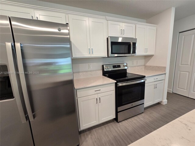 6001 Woods Edge Cir, Riviera Beach, FL 33410 - kitchen featuring stainless steel appliances, white cabinets, wood finished floors, and light stone countertops